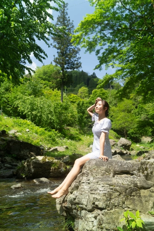 新緑が美しい森の中、渓流沿いの大きな岩に座る若い女性の姿