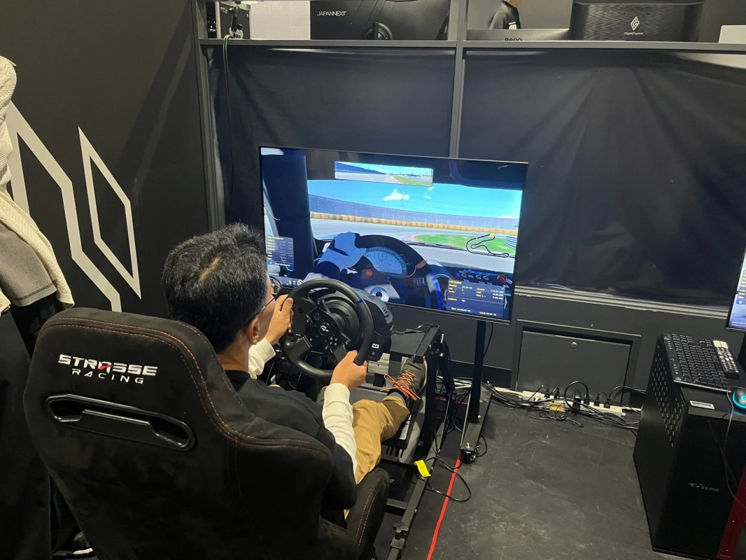 男性がレーシングシミュレーターに座り、大型モニターで本格的なドライブゲームを楽しんでいます。